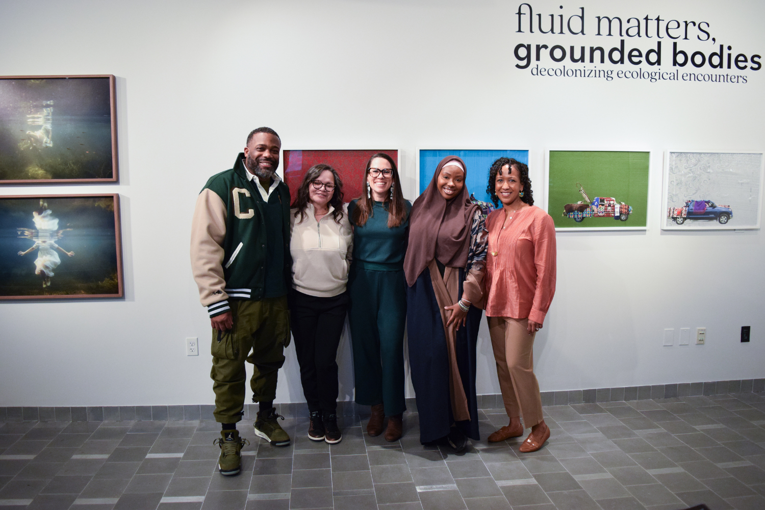 Photo shows five people smiling for a group photo at Gallery 360. The show on view is "Fluid Matters, Grounded Bodies."