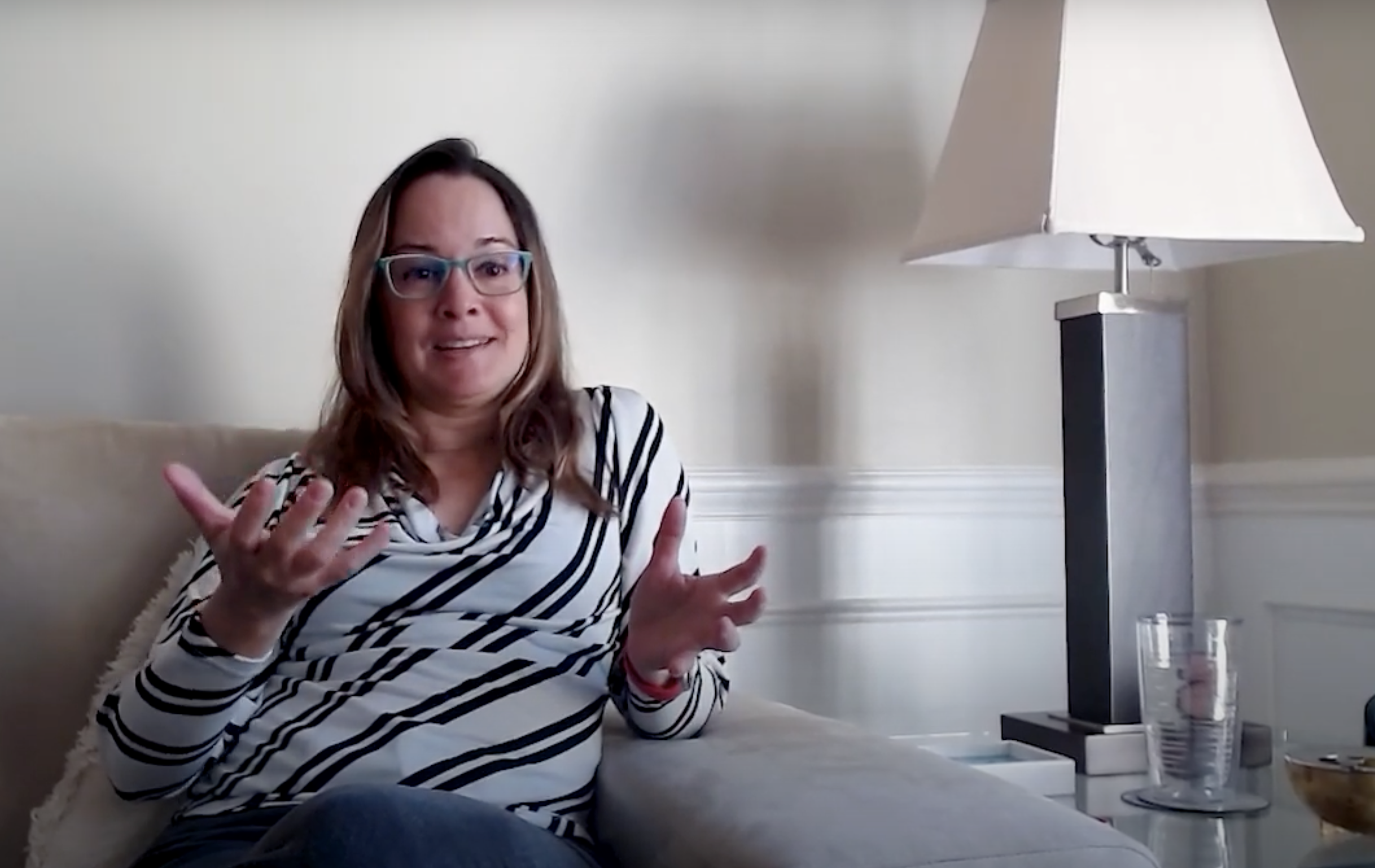 Photo shows Dr. Adriana de Souza e Silva sitting on a couch. She is gesticulating and talking about the history of mobile communication.