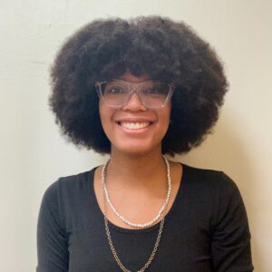 Headshot image of Melania Diaz. She is smiling and wears translucent framed glasses.
