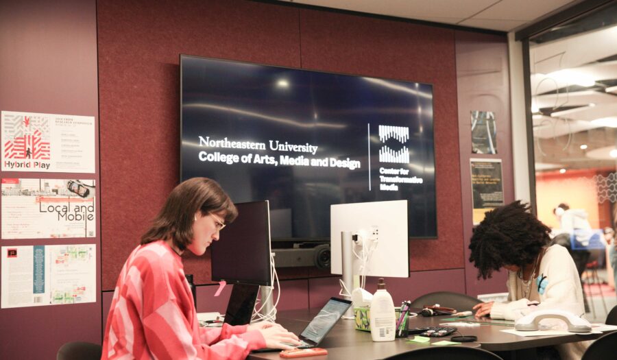 Evelyn and Melania work together in the Center for Transformative Media office. Behind them is the Center's logo.