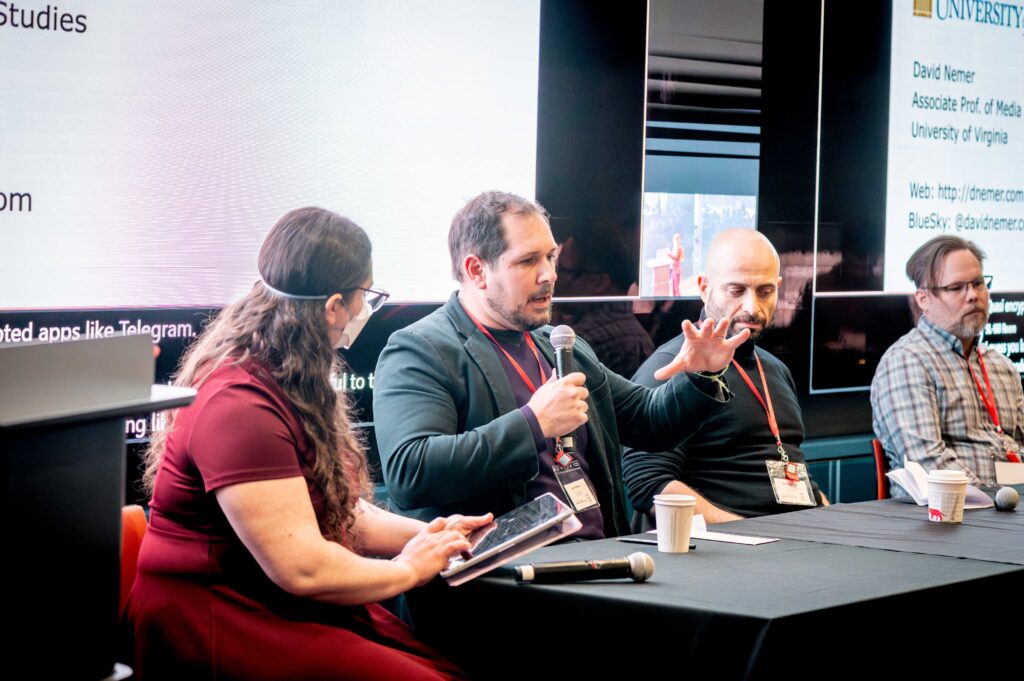 Image of Prof. John Wihbey speaking at the Center for Transformative Media's launch event, "Media in Motion," on Mar. 28, 2025. Wihbey is speaking into a microphone, and there is a bright TV behind him. He is sitting next to faculty members Michael Ann DeVito, Sina Fazelpour, and Derek Curry.