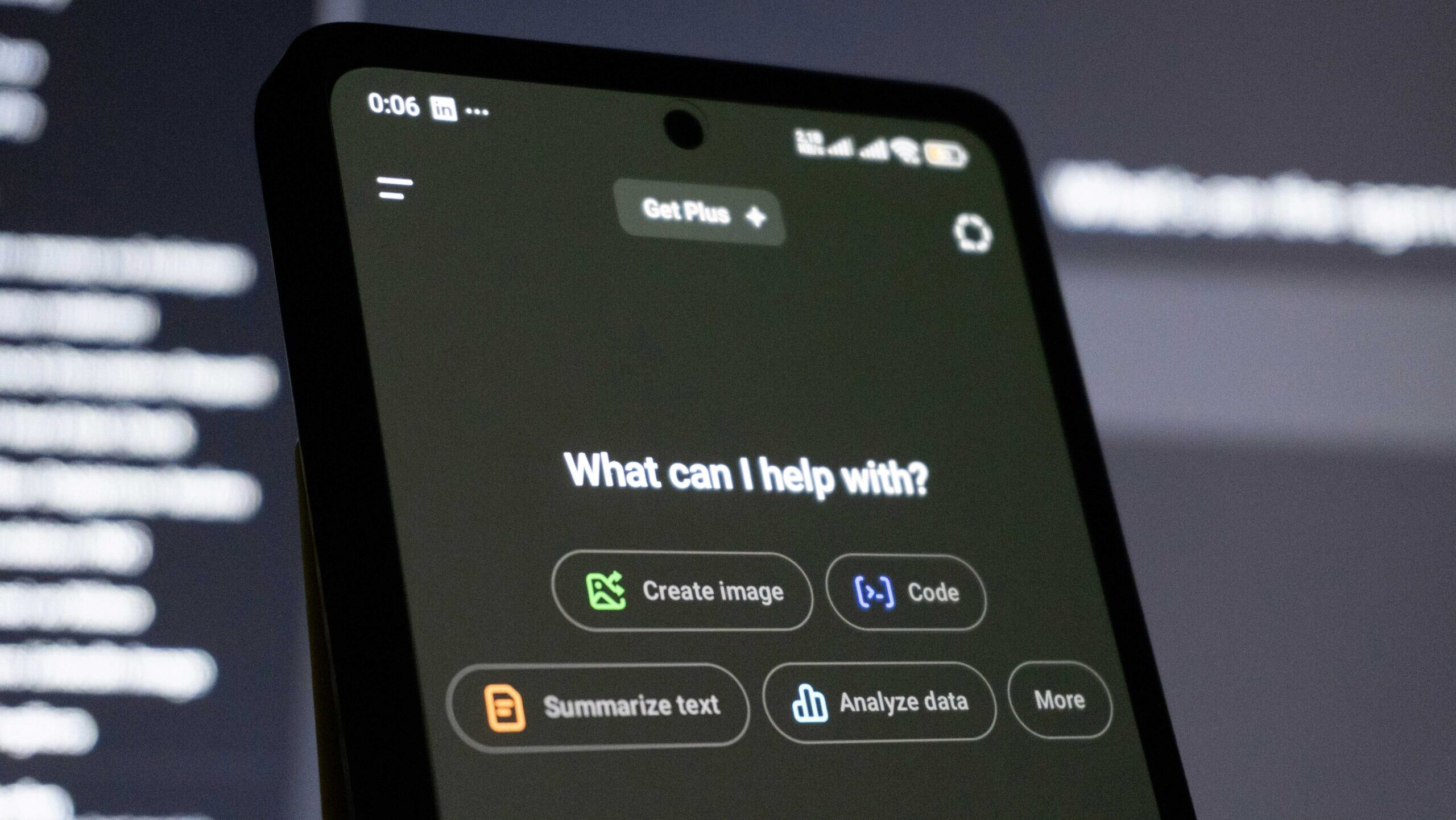 Photo that shows a phone screen with a genAI software screen saying "What can I help with?" There are several option buttons, including "Generate Image," "Code," "Summarize text," "Analyze data," and "more."