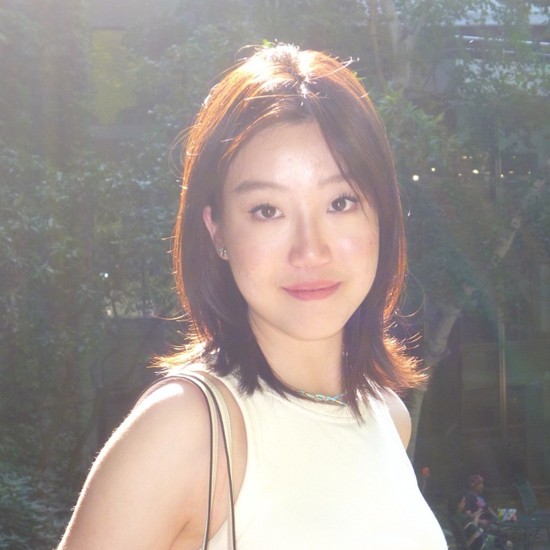 Image of student Hedan (Helena) Chen. She is wearing a white tshirt and smiling slightly. Standing in front of trees.